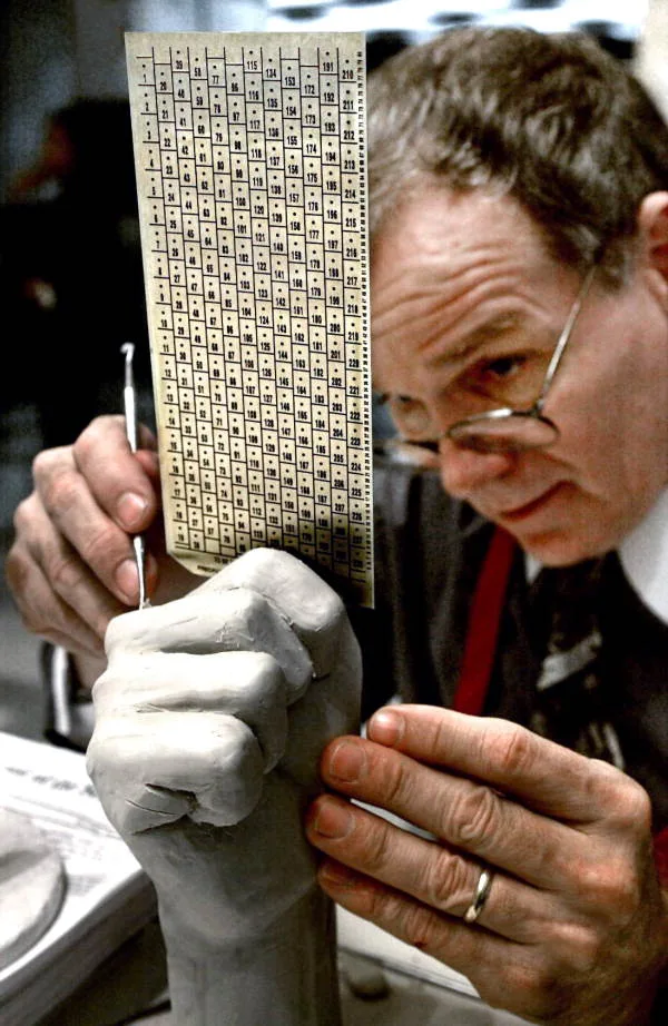 An election official holds a Votomatic punch card ballot up to the light, closely examining its rows of numbered punch positions for stray or incomplete marks.