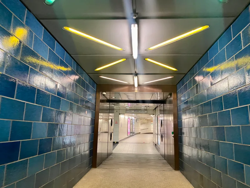 A tiled passageway inside Bank station connecting to Monument station, with a sign pointing toward trains and the public subway.