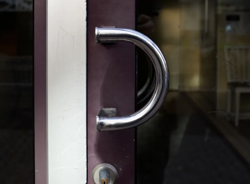 A large chrome D-shaped pull handle mounted on a glass door, its curve and size inviting a hand to wrap around it.