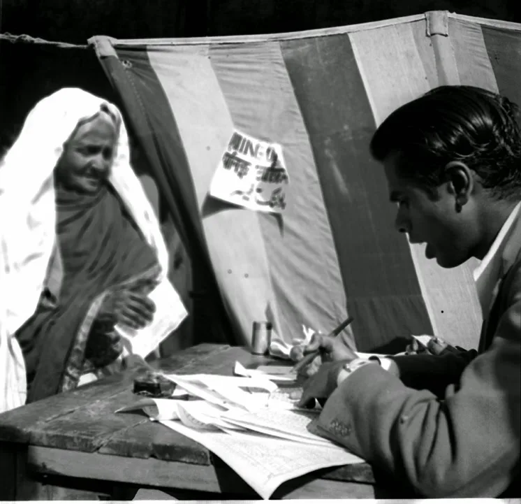 An elderly woman being identified by a polling officer at a striped-tent polling booth during India's first general election, 1952.