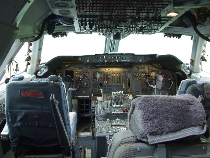 The three-crew flight deck of a classic KLM Boeing 747-200, showing the captain and first officer seats and the overhead panel facing the flight engineer's station.