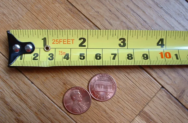 A retractable tape measure printed with both feet and inches on one edge and centimetres on the other, two coins resting below it for scale.