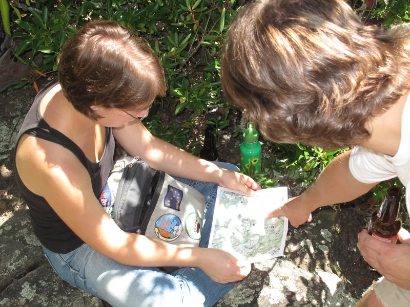 Two hikers pointing at a paper trail map while planning a route outdoors