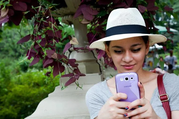 A woman in a sun hat casually holding up a smartphone to take a photograph outdoors