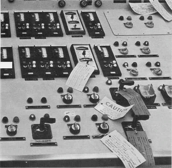 Close-up of the TMI-2 control panel showing rows of switches and indicator lights, several covered with paper maintenance tags including one reading CAUTION.